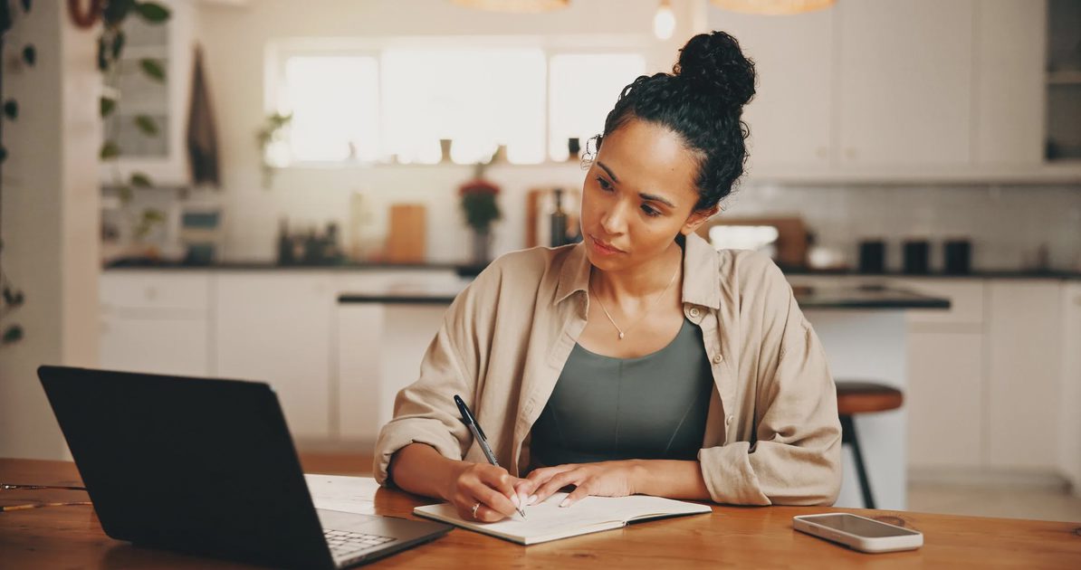 Person using a laptop and handwritten notes to brainstorm ideas for a personal project.